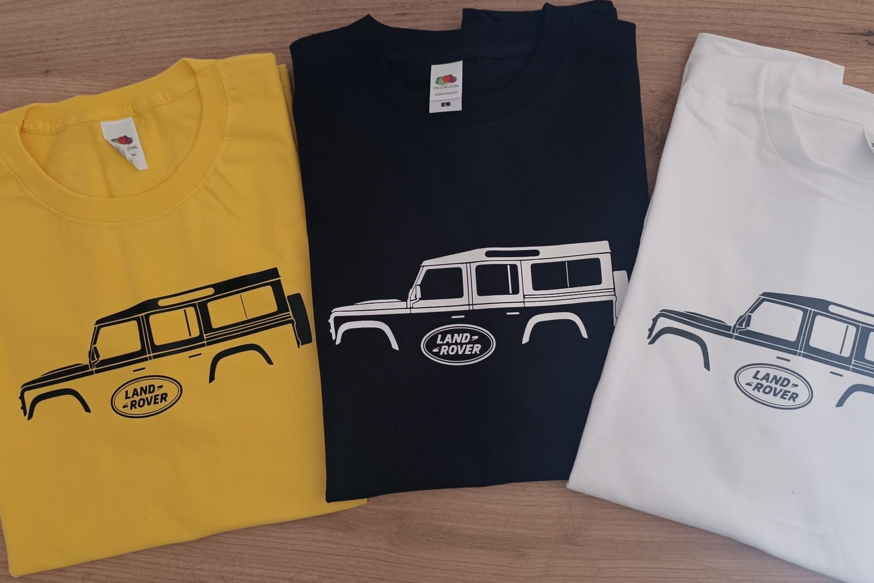 Drei T-Shirts in Gelb, Schwarz und Weiß mit einem Land Rover Defender 110 in Schwarz.