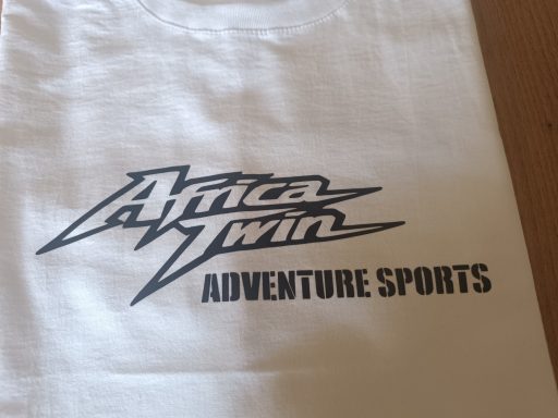 Weißes T-Shirt mit dem Aufdruck "Africa Twin Adventure Sports" in stylisierter Schrift.