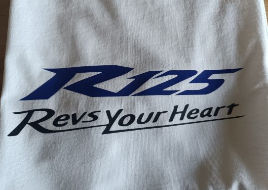 Logo mit der Aufschrift „R125“ und „Revs Your Heart“ in blauer und schwarzer Schrift.