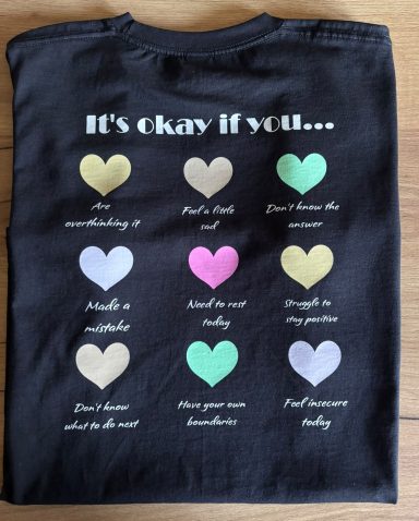 Schwarzes T-Shirt mit bunten Herzen und verschiedenen Aussagen darüber, wie man sein kann.