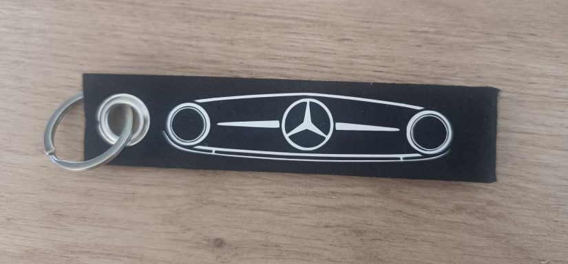 Schwarzer Schlüsselanhänger mit dem markanten Kühlergrill des Mercedes Benz O319 Panoramabus